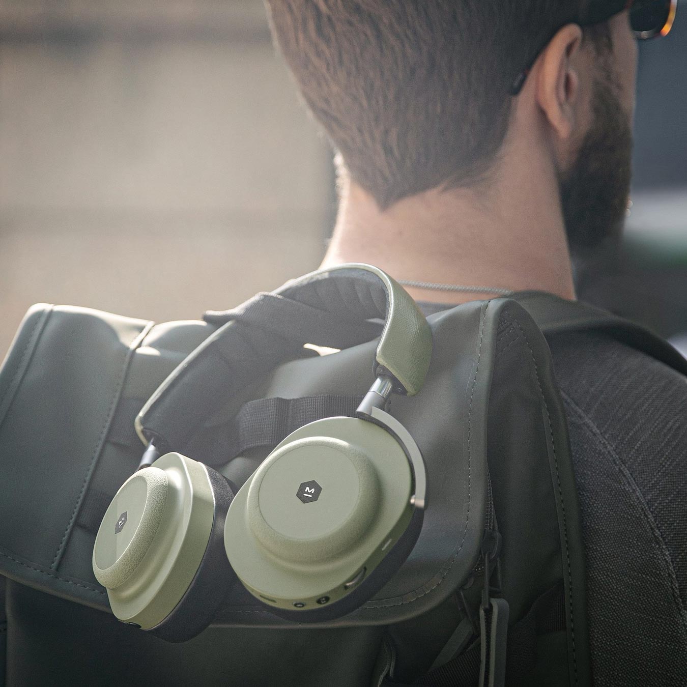 Man facing away from the camera holding a backpack, with moss green and black MG20 Wireless Gaming Headphones hanging from the backpack handle | gallery MG20GR8