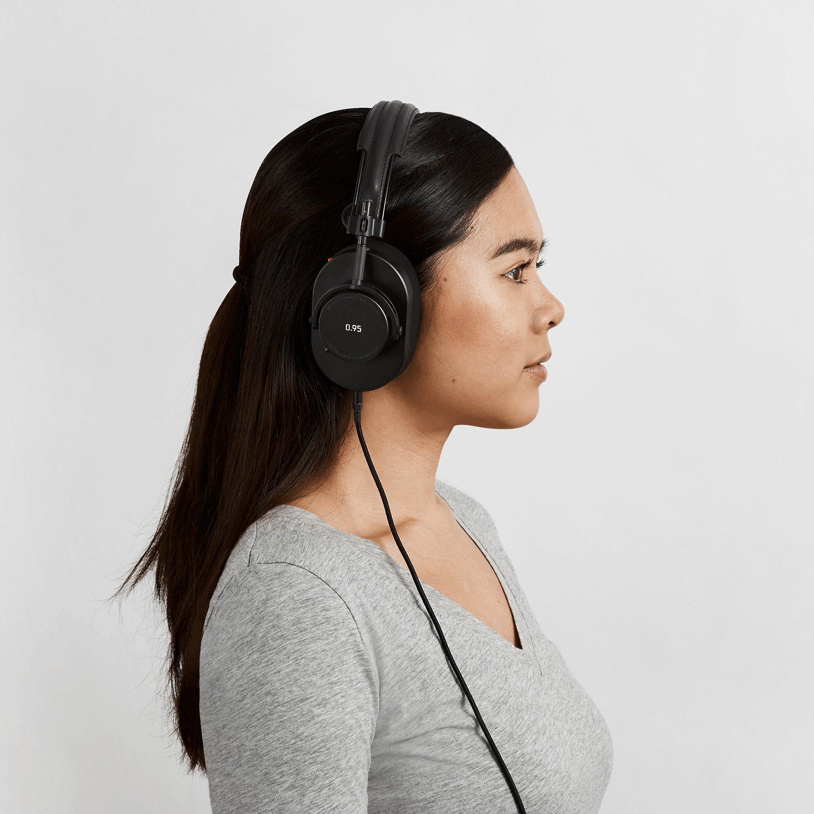 Profile of woman with black hair and a grey v-neck shirt wearing black leather and metal MH40 Wireless Headphones with Leica 0.95 on the ear cup and optional 3.5mm audio cable attached | gallery MH40B-95