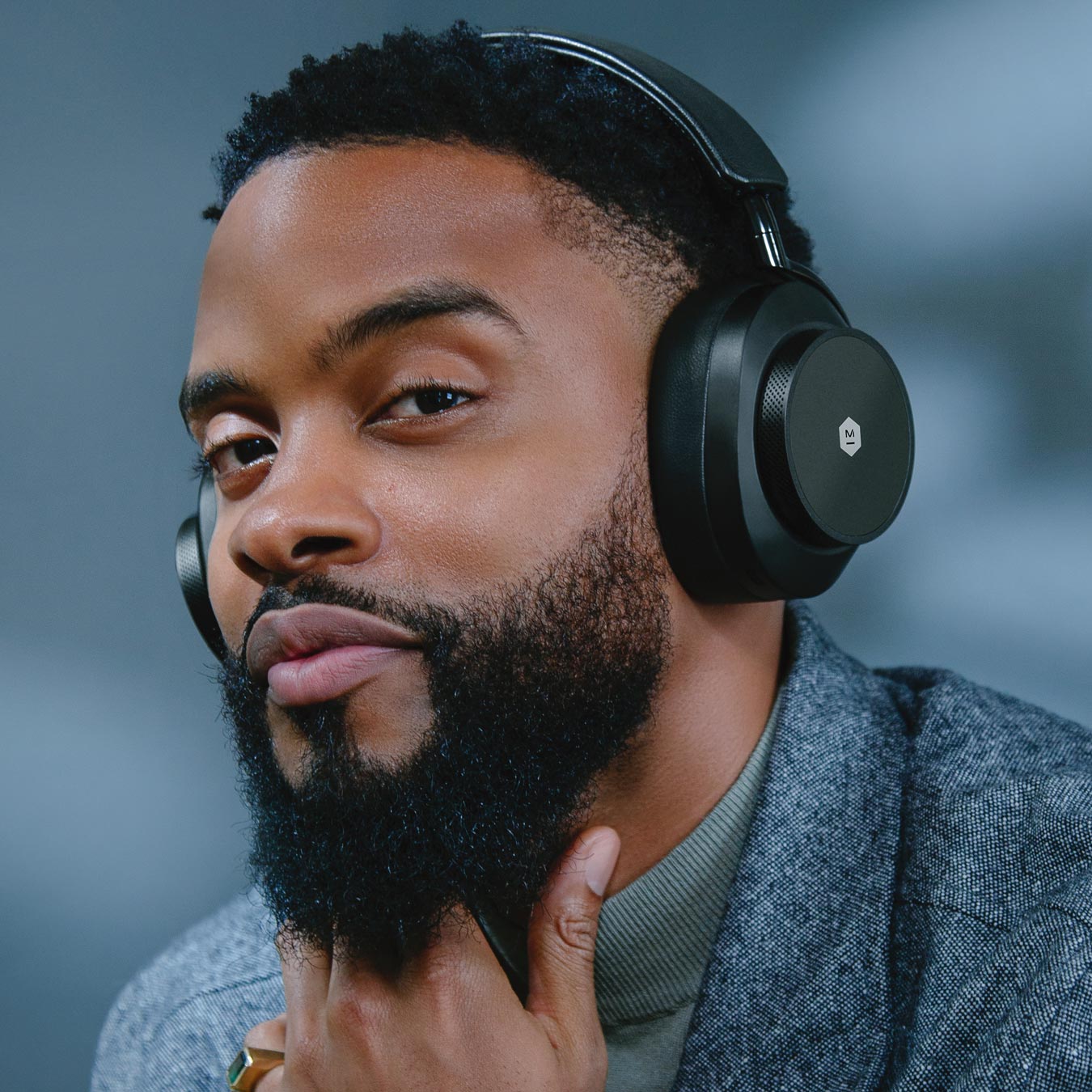 Close up of a bearded man wearing a grey coat wearing black MW75 Active Noise-Cancelling Headphones against a grey background | gallery MW75B1