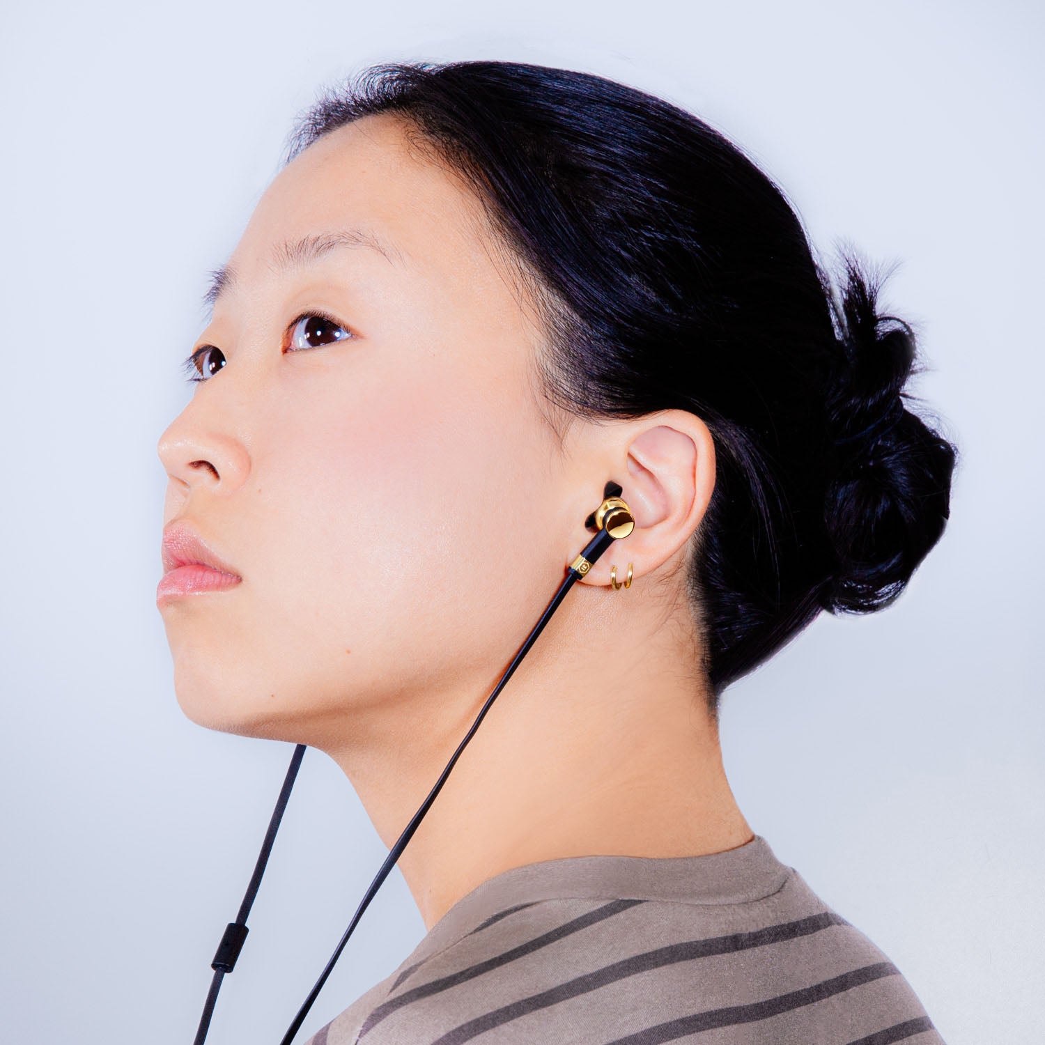 Profile of a woman with dark hair and striped shirt wearing wired black and gold  ME05 Earphones | gallery ME05GD-MK2