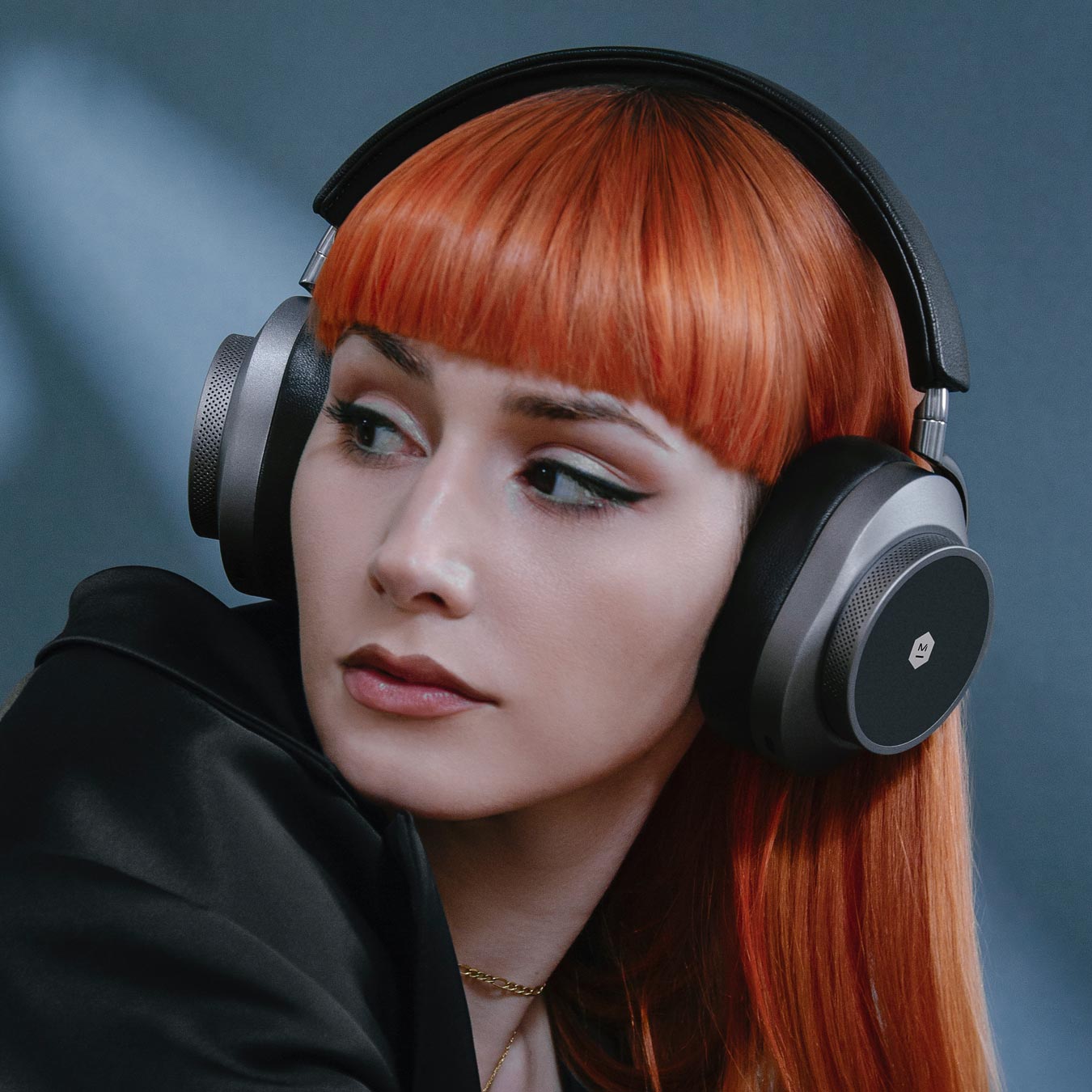 Close up of a woman with orange hair wearing gunmetal and black MW75 Active Noise-Cancelling Headphones against a grey background | gallery MW75G1